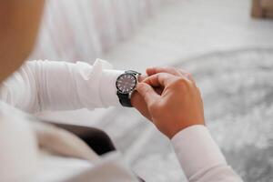 A man is wearing a watch and looking at it. The watch is black and has a silver band photo
