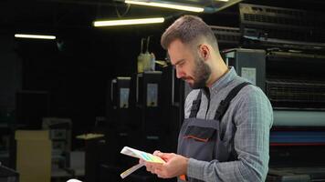 Worker in a printing and press center uses a color palette to select the correct shade of color from CMYK printed sheet video