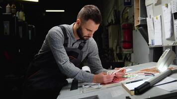 Worker in a printing and press center uses a color palette to select the correct shade of color from CMYK printed sheet video