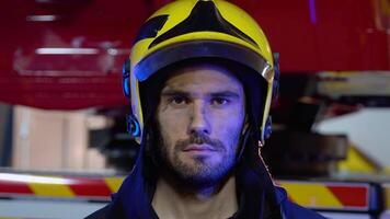 Tired firefighter in protective uniform looking at camera near fire engine after extinguishing a fire video