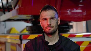 Tired firefighter in protective uniform looking at camera while standing near fire engine after extinguishing a fire video