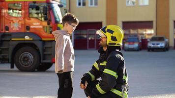 Firefighter in uniform is with a little boy at fire station video