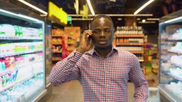 Handsome black man walking and looking around in supermarket and speaks on the phone with his wife video