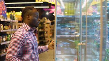Black man shopping in beverage section at supermarket, chooses cold fizzy drink video