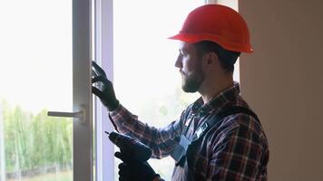 Workman in uniform installing or adjusting plastic windows in the living room at home video
