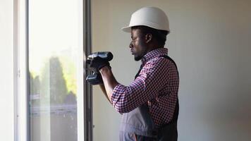 African construction worker installing pvc window or door in house. Handyman fixing the window with screwdriver video
