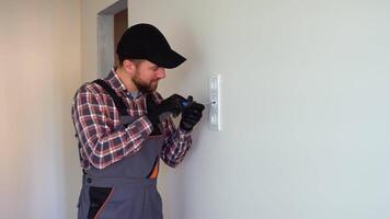 Professional electrician in overalls and black cap installing a socket on a wall video