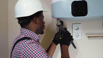 Professional black plumber in uniform installing a boiler in new home video
