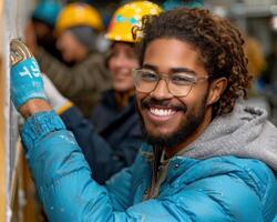 A young man wearing safety glasses smiles while working on a wall photo