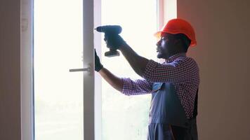 African construction worker installing window in house. Handyman fixing the window with screwdriver video