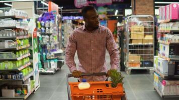 African american man walking with shopping trolley while doing shopping in grocery store video