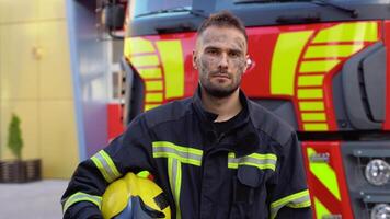 Tired fireman in protective uniform looking at camera while standing near fire engine on station video