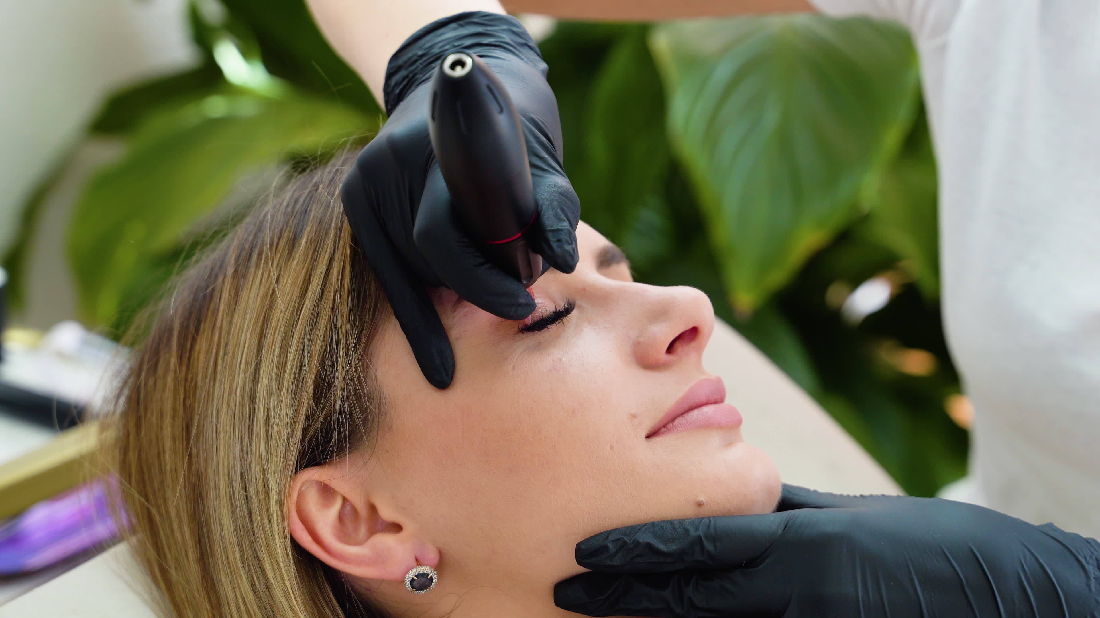 Young girl applying permanent eyeliner in beauty studio. Permanent make