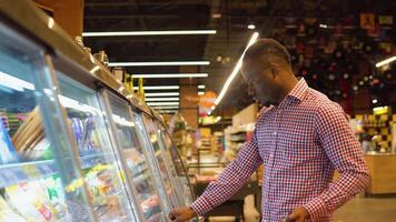 Black man shopping cheese in grocery store. A man chooses the French cheese brie or camembert video