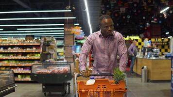 African american man walking with shopping trolley while doing shopping in grocery store video
