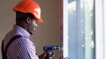 African american workman in overalls installing or adjusting plastic windows in the living room at home video
