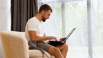 Handsome man with broken leg using laptop on sofa video