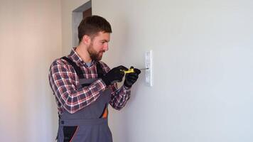 Professional electrician in overalls and black cap installing a socket on a wall video