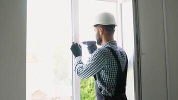Workman in uniform installing or adjusting plastic windows in the living room at home video