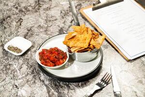 Tortilla Chips with Tomato Salsa Sauce, dip, fork and knife served in plate isolated on marble background side view of hong kong food photo