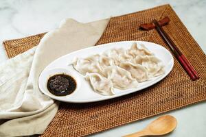 Steamed Dumplings with black truffle vinaigrette Sauce, chopsticks and spoon served in dish isolated on napkin side view of Chinese food photo