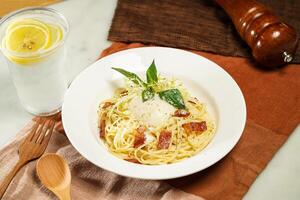 with lemonade, wooden spoon Linguine Carbonara with Soft Boiled Egg or Hot spring egg carbonara pasta and fork served in plate isolated on napkin and dining table side view of italian food photo