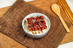 Teriyaki eel donburi with rice, chopsticks and spoon served in bowl isolated on napkin side view of Japanese food photo