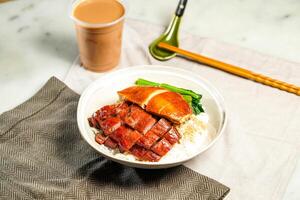 BBQ Pork and Soya Chicken with Rice with milk kopi chopsticks and spoon served in bowl isolated on napkin side view of hong kong food on marble background photo