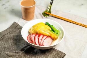 Chinese Sausage and Poached Chicken Leg with Rice with milk kopi chopsticks and spoon served in bowl isolated on napkin side view of hong kong food on marble background photo