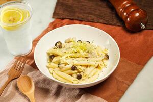 Penne with Wild Mushrooms Pasta in Cream Sauce with lemonade, wooden spoon and fork served in plate isolated on napkin and dining table side view of italian food photo