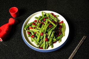 Dry fried String Beans with Minced Pork and red chilli pepper with chopsticks served in dish on dark background top view of hong kong food photo