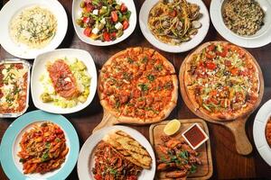 Assortment of fastfood with pizza, Lasagne, Bolognese, chicken wings, greek and caesar salad, Fettuccini, Risotto, Spaghetti served in dish isolated on wooden table top view of italian fast food photo