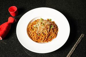 Noodles in Soy and Scallion Oil with chopsticks served in dish on dark background top view of hong kong food photo
