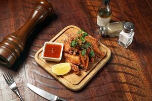 Secret Spicy Chicken Wings with chilli sauce and lime slice served in dish isolated on wooden table top view of italian fast food photo