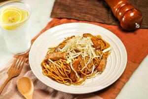 Spaghetti Noodles with Pork Chop in Swiss Sauce with lemonade, wooden spoon and fork served in plate isolated on napkin and dining table side view of italian food photo