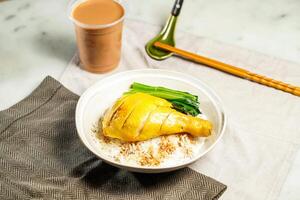 Poached Chicken Leg with Rice with milk kopi chopsticks and spoon served in bowl isolated on napkin side view of hong kong food on marble background photo