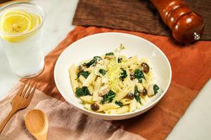 Penne with Spinach and Mushroom with lemonade, wooden spoon and fork served in plate isolated on napkin and dining table side view of italian food photo
