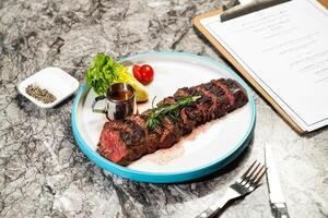 grilled Beef belly steak slice with butter, lettuce, cherry tomato, dip, fork and knife served in plate isolated on marble background side view of hong kong food photo