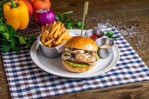 Chicken and Avocado Burger with french fries, ketchup, mayo dip, tomato, onion, capsicum, coriander, served in dish isolated on napkin side view of italian fastfood on wooden table photo