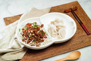 Sichuan sesame meat floss rice noodles with Steamed dumplings chopsticks and spoon served in dish isolated on napkin side view of Chinese food photo