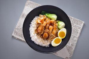 Abalone fish maw with rice with boiled egg and pickled vegetables served in bowl isolated on napkin top view of chinese food on grey background photo