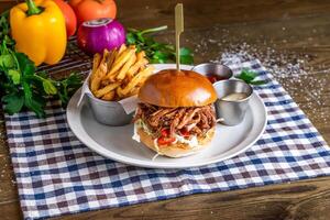 Pulled Pork Burger with french fries, ketchup, mayo dip, tomato, onion, capsicum, coriander, served in dish isolated on napkin side view of italian fastfood on wooden table photo