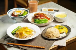 Boneless Hainanese Chicken Rice, Roasted Duck, Poached Chicken, BBQ Pork with Fried Egg, baby kailan, milk kopi and chopsticks isolated on napkin table side view of assorted asian foods photo
