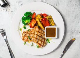 Grilled Chicken Breast Bowl with broccoli, tomato, lettuce, sauce, and lemon served in bowl isolated on background top view of italian food photo