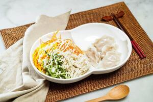 Japanese cold shredded chicken noodles with wasabi lime sauce and Steamed dumplings, chopsticks and spoon served in dish isolated on napkin side view of Chinese food photo