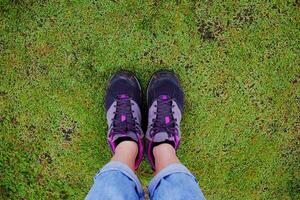 Top view selfie of woman feet and black sneaker stand on the grass field in tropical garden photo