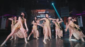 Diverse group of dancers performing on stage with dynamic lighting and a vibrant backdrop, showcasing modern dance video