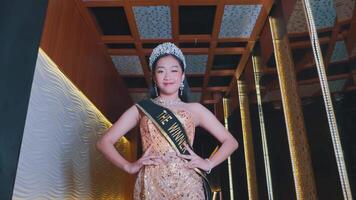 Elegant beauty queen in a pageant sash posing confidently indoors with a decorative backdrop. video
