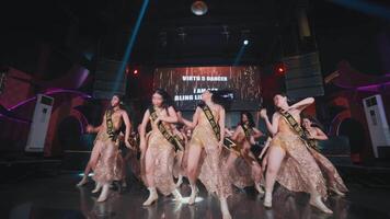 Group of dancers performing on stage with dynamic lighting and a digital screen displaying text in the background video