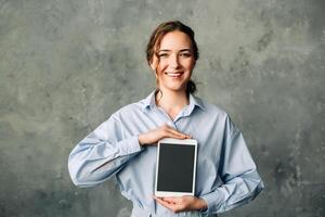 Young businesswoman smiling and holding a tablet with a blank screen. Perfect for showcasing technology, digital advertising, or app promotion. Ideal for professional and tech-related content photo